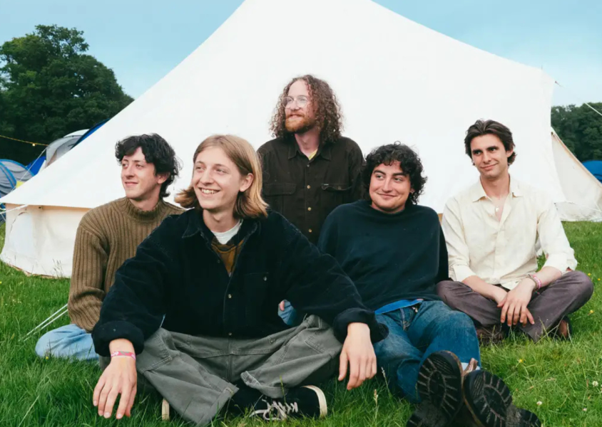 Band looking happy in front of a tent whilst touching grassx